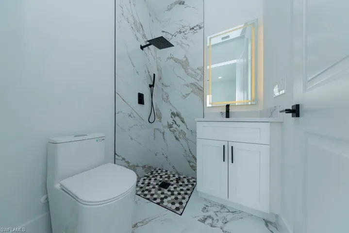 Bathroom featuring vanity, a marble finish shower, and light marble finish floors