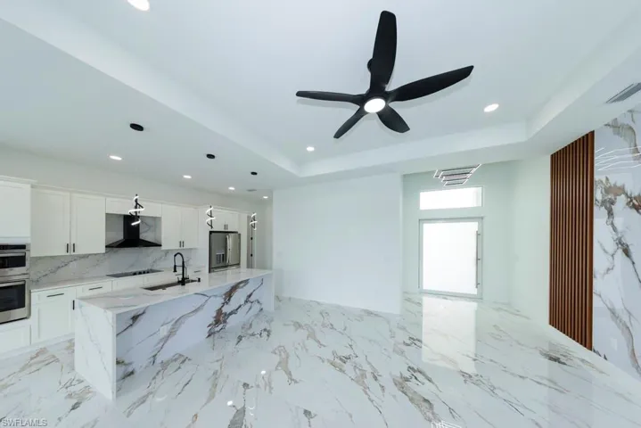 Unfurnished living room featuring recessed lighting, a raised ceiling, light marble finish flooring, and a ceiling fan