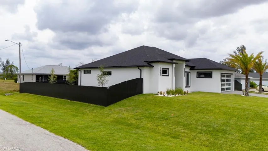 Rear view of house with stucco siding, an attached garage, roof with shingles, and driveway