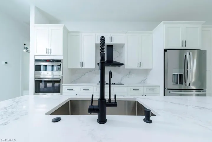 Kitchen featuring stainless steel appliances, white cabinetry, light stone countertops, and tasteful backsplash