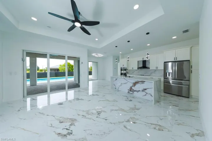 Living room featuring a tray ceiling, light marble finish floors, recessed lighting, and ceiling fan