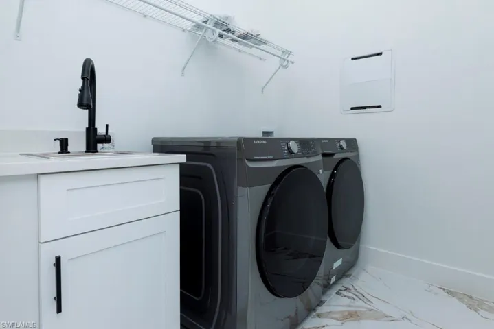 Washroom with light marble finish flooring, independent washer and dryer, and cabinet space