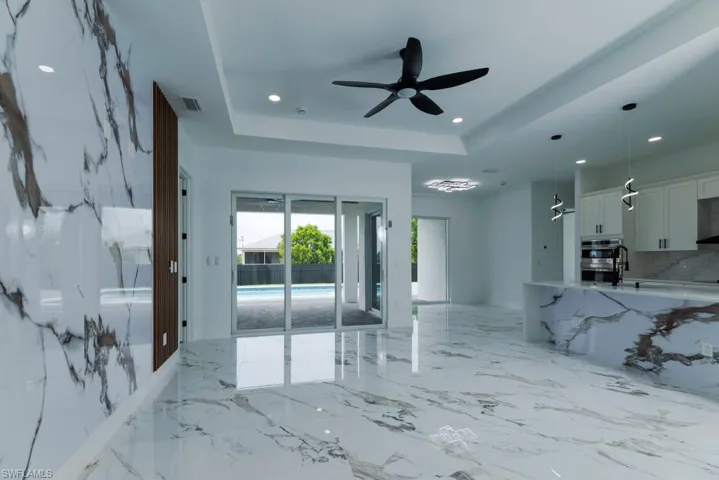 Living area featuring a raised ceiling, light marble finish flooring, recessed lighting, and a ceiling fan