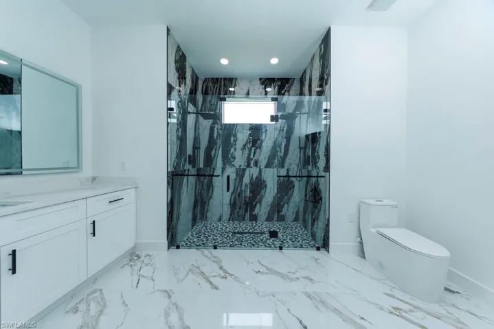 Bathroom featuring vanity, a marble finish shower, light marble finish flooring, and recessed lighting