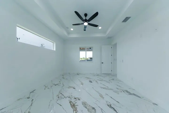 Empty room with marble finish flooring, a raised ceiling, recessed lighting, and a ceiling fan