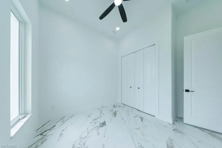 Unfurnished bedroom with multiple windows, a closet, a ceiling fan, light marble finish floors, and recessed lighting