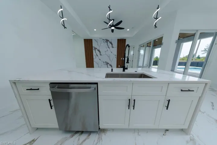 Kitchen with light marble finish flooring, light stone countertops, white cabinetry, dishwasher, and recessed lighting