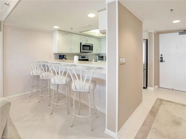 Kitchen with white cabinets, stainless steel appliances, kitchen peninsula, light tile patterned flooring, and a breakfast bar area