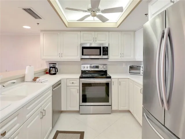Kitchen with light tile patterned floors, appliances with stainless steel finishes, sink, white cabinetry, and ceiling fan