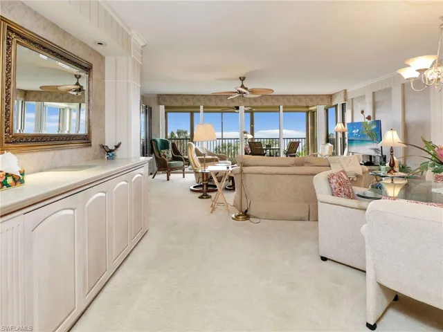 Carpeted living room featuring a wealth of natural light and ceiling fan with notable chandelier