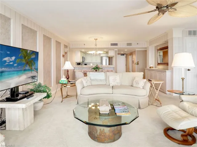 Carpeted living room with ceiling fan with notable chandelier and crown molding