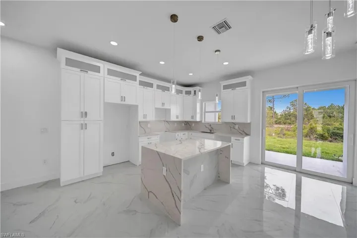 Kitchen featuring light marble finish flooring, a center island, a sink, recessed lighting, and glass insert cabinets