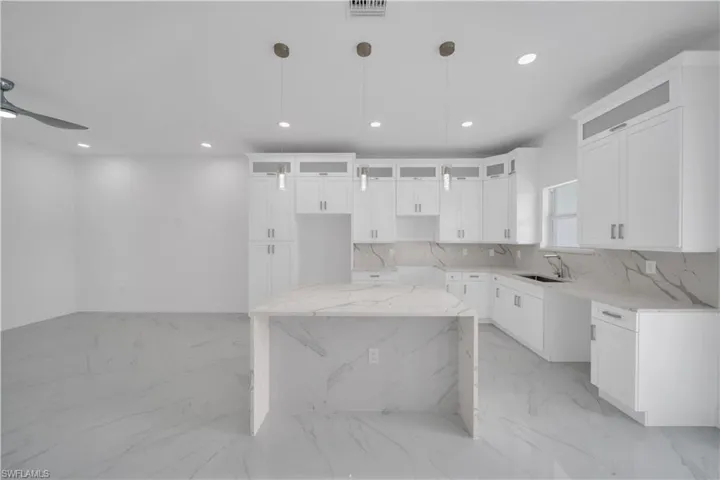Kitchen with recessed lighting, a kitchen island, light marble finish floors, glass insert cabinets, and pendant lighting