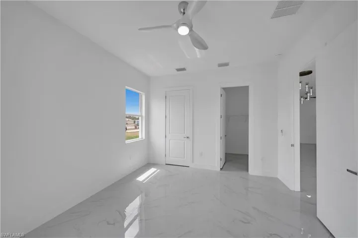 Unfurnished bedroom with marble finish flooring, baseboards, a ceiling fan, and a spacious closet