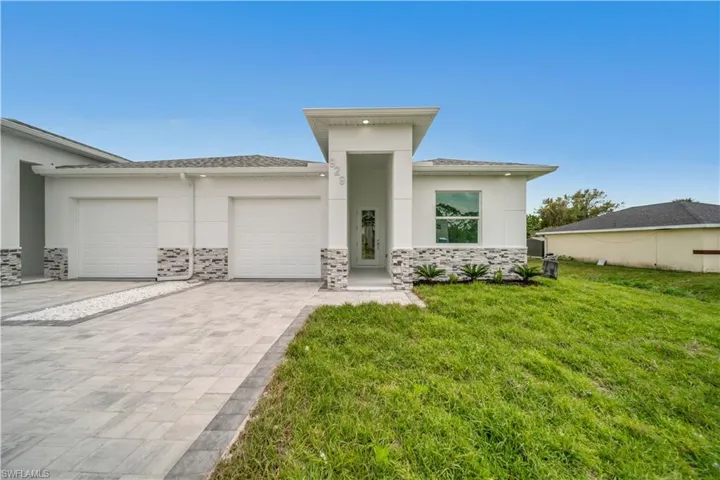 Prairie-style home with stucco siding, an attached garage, stone siding, and decorative driveway