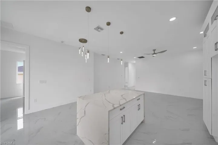 Kitchen with open floor plan, white cabinets, light stone countertops, a ceiling fan, and light marble finish flooring
