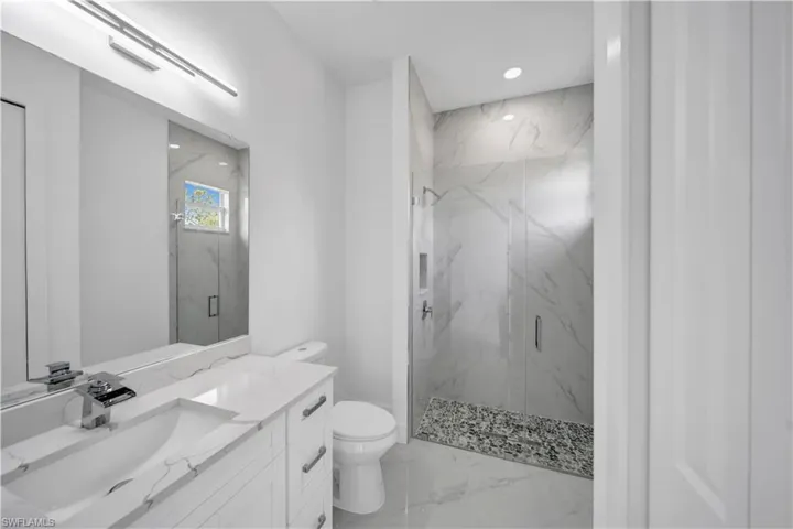Bathroom with toilet, a marble finish shower, vanity, marble finish floors, and recessed lighting
