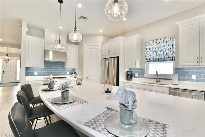 Kitchen with a breakfast bar, stainless steel appliances, white cabinetry, and light stone counters
