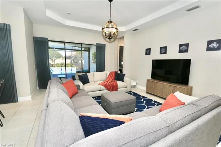 Living room with a raised ceiling, light tile patterned flooring, and suspended lighting