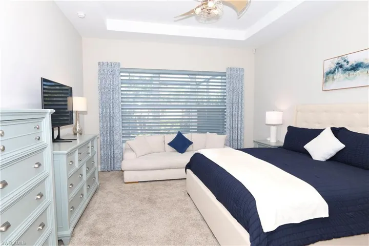 Bedroom featuring a tray ceiling, light carpet, and ceiling fan