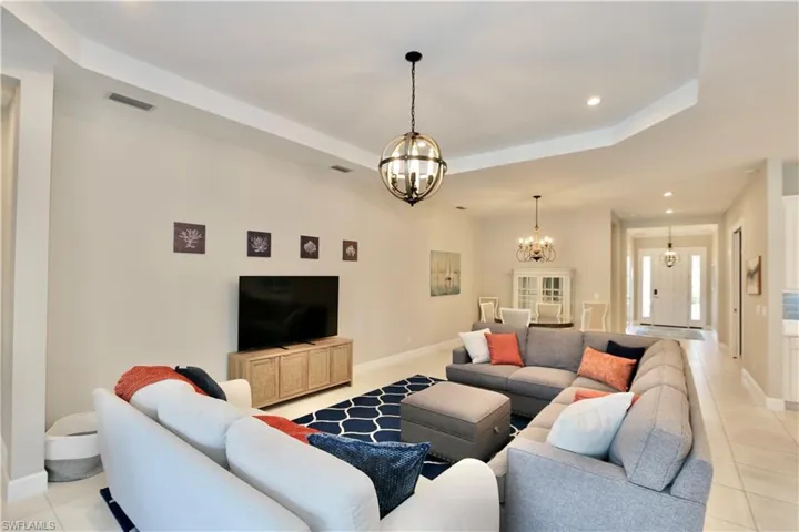 Living area featuring light tile patterned flooring, suspended lighting, and a tray ceiling