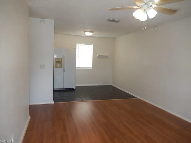 Empty room with a textured ceiling, ceiling fan, and dark wood-type flooring