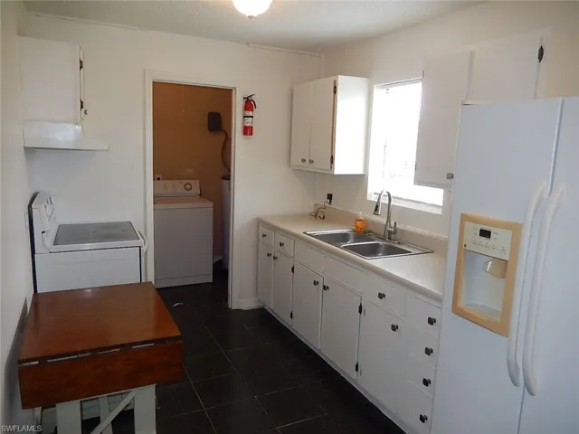 Kitchen with white refrigerator with ice dispenser, white cabinetry, light countertops, washer / dryer, and a textured ceiling