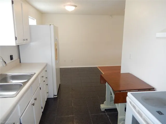Kitchen with white cabinetry, light countertops, white appliances, a textured ceiling, and dark tile patterned floors