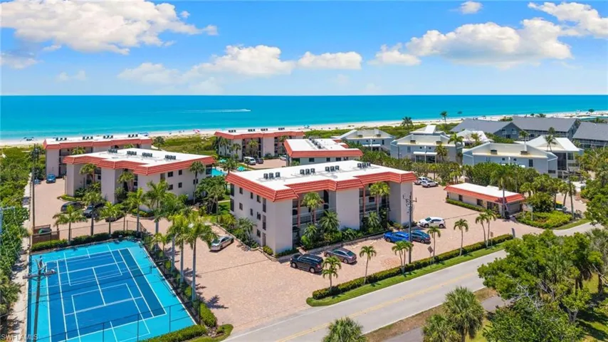 Coastal property featuring multiple residential buildings with red tile roofs, a tennis court, and lush landscaping