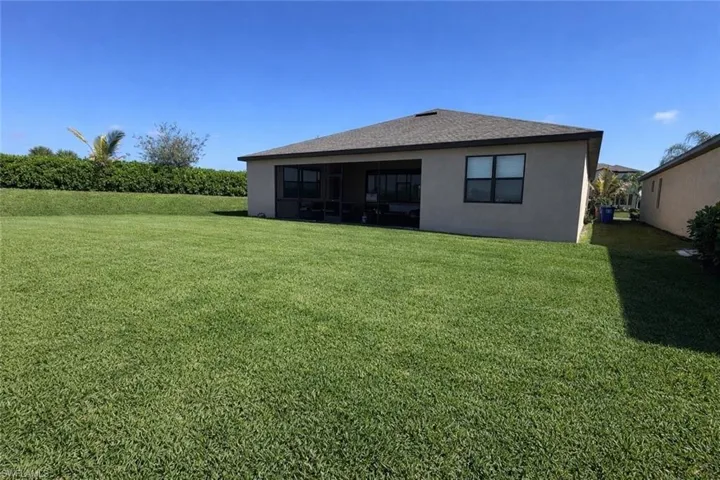 Rear view of house with a lawn, stucco siding, a sunroom, and roof with shingles