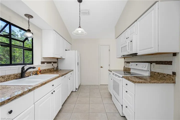 Kitchen featuring white appliances, backsplash, white cabinets, vaulted ceiling, and light tile patterned floors