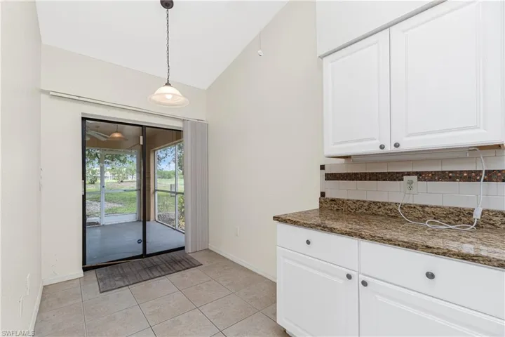 Kitchen with decorative backsplash, white cabinetry, decorative light fixtures, light tile patterned floors, and lofted ceiling
