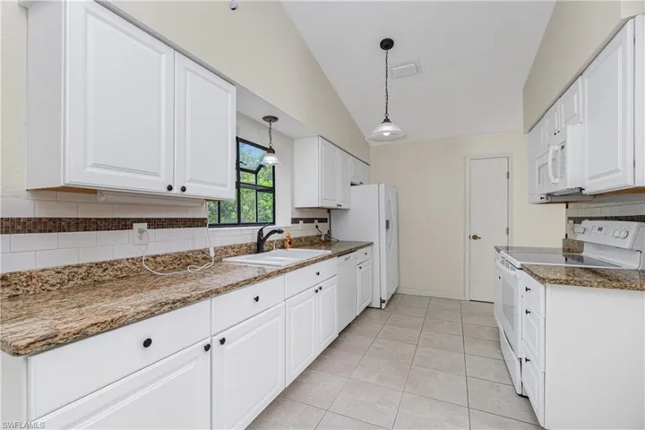Kitchen featuring white appliances, vaulted ceiling, tasteful backsplash, white cabinets, and light tile patterned floors