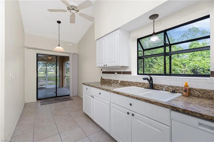 Kitchen with white cabinets, healthy amount of natural light, decorative light fixtures, vaulted ceiling, and light tile patterned flooring