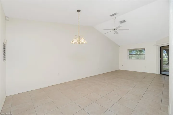 Empty room featuring a chandelier, lofted ceiling, light tile patterned floors, and a ceiling fan