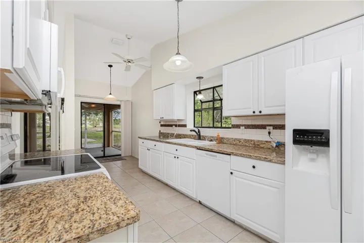 Kitchen with white appliances, lofted ceiling, white cabinets, light tile patterned floors, and ceiling fan