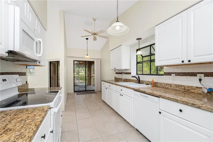 Kitchen featuring white appliances, light tile patterned floors, a ceiling fan, decorative backsplash, and high vaulted ceiling