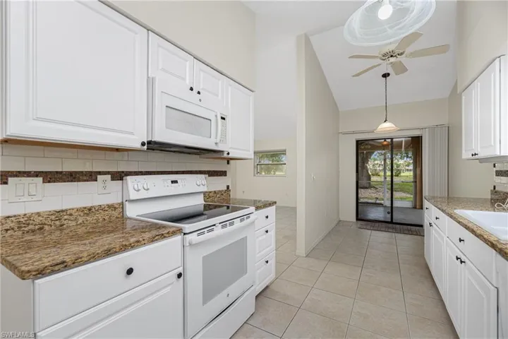 Kitchen with white appliances, decorative backsplash, light tile patterned floors, healthy amount of natural light, and high vaulted ceiling