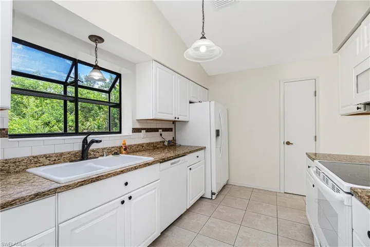 Kitchen with white appliances, lofted ceiling, tasteful backsplash, white cabinetry, and hanging light fixtures