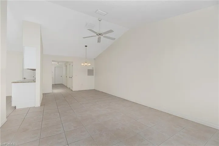 Unfurnished living room with a ceiling fan, light tile patterned floors, a chandelier, and high vaulted ceiling