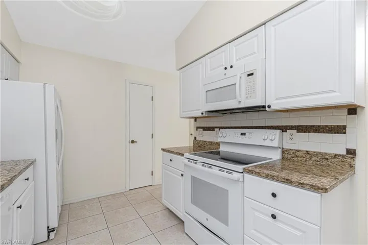 Kitchen featuring white appliances, backsplash, white cabinetry, and light tile patterned floors
