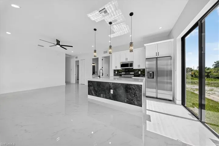 Kitchen with light marble finish floors, pendant lighting, appliances with stainless steel finishes, a kitchen island with sink, and white cabinets