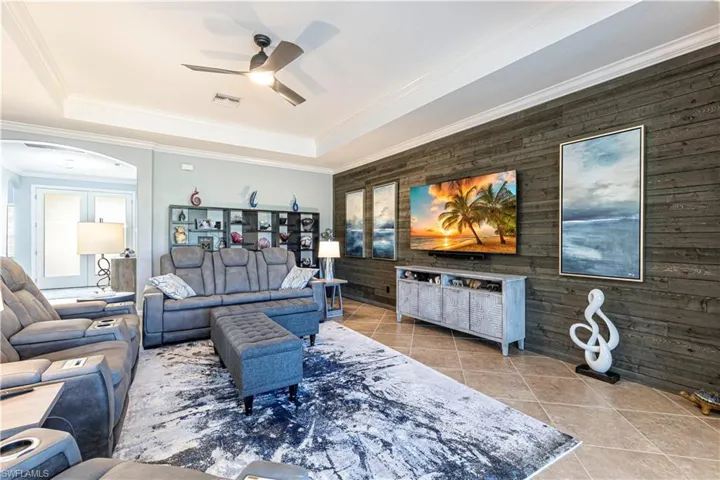 Tiled living room with a raised ceiling, crown molding, wooden walls, and ceiling fan