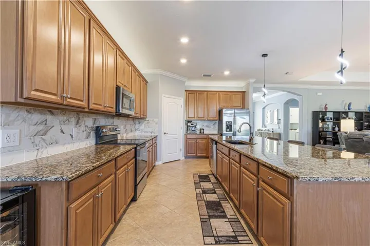 Kitchen featuring stone countertops, pendant lighting, sink, ornamental molding, and appliances with stainless steel finishes