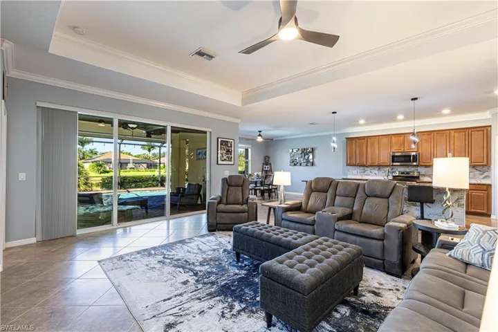 Living room with ceiling fan, a raised ceiling, crown molding, and light tile patterned floors
