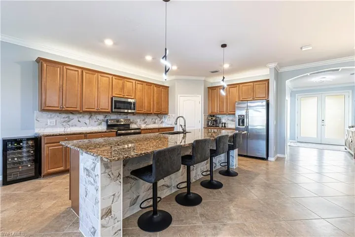 Kitchen featuring pendant lighting, beverage cooler, a kitchen island with sink, stainless steel appliances, and crown molding