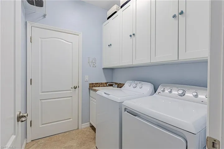 Laundry area with washer and clothes dryer, cabinets, sink, and light tile patterned floors