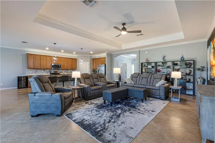 Tiled living room with ornamental molding, ceiling fan, and a tray ceiling