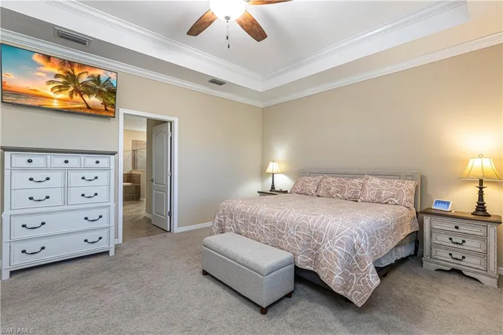 Bedroom with ceiling fan, light colored carpet, a tray ceiling, and crown molding