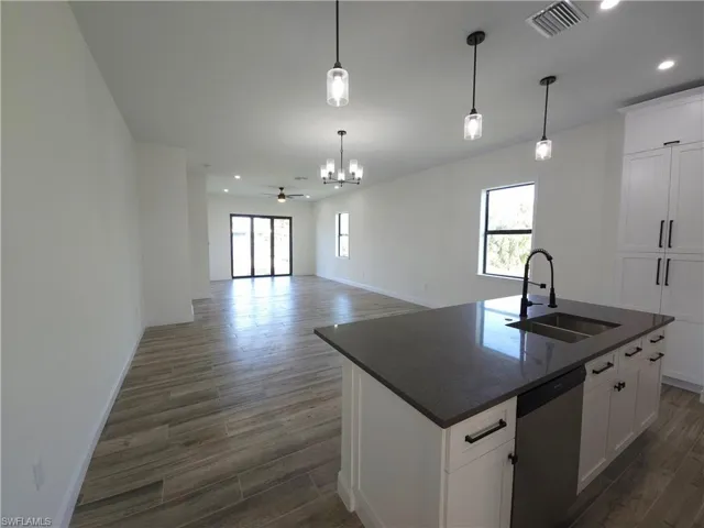 Spacious open-concept interior featuring wood-finish flooring, a kitchen island with a dark countertop and undermount sink, white cabinetry with dark hardware, and pendant lighting